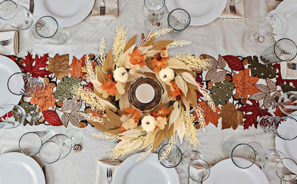 Autumn wreath with pumpkins, leaves, and flowers centered on a table runner with fall leaf motifs, set for a meal.