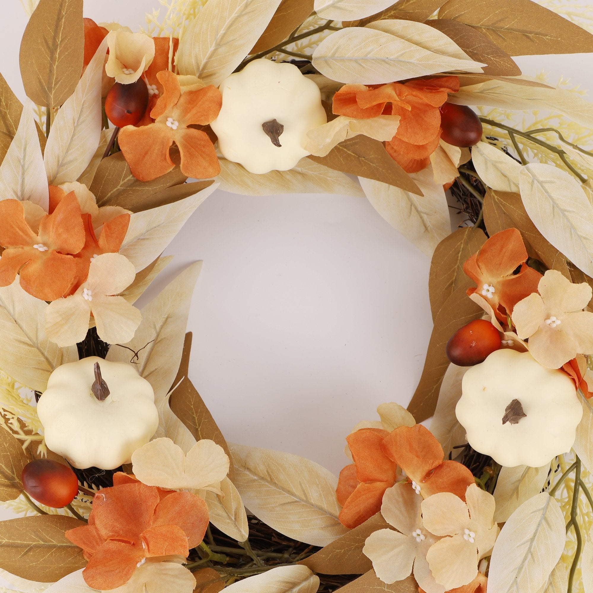 Artificial fall wreath with white pumpkins, orange and yellow leaves, and flowers, set against a white background.