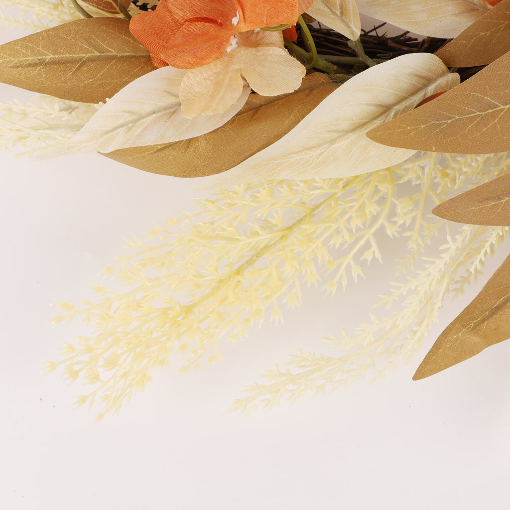 Close-up of an artificial autumn wreath with brown and cream leaves, orange flowers, and delicate cream foliage against a white background.