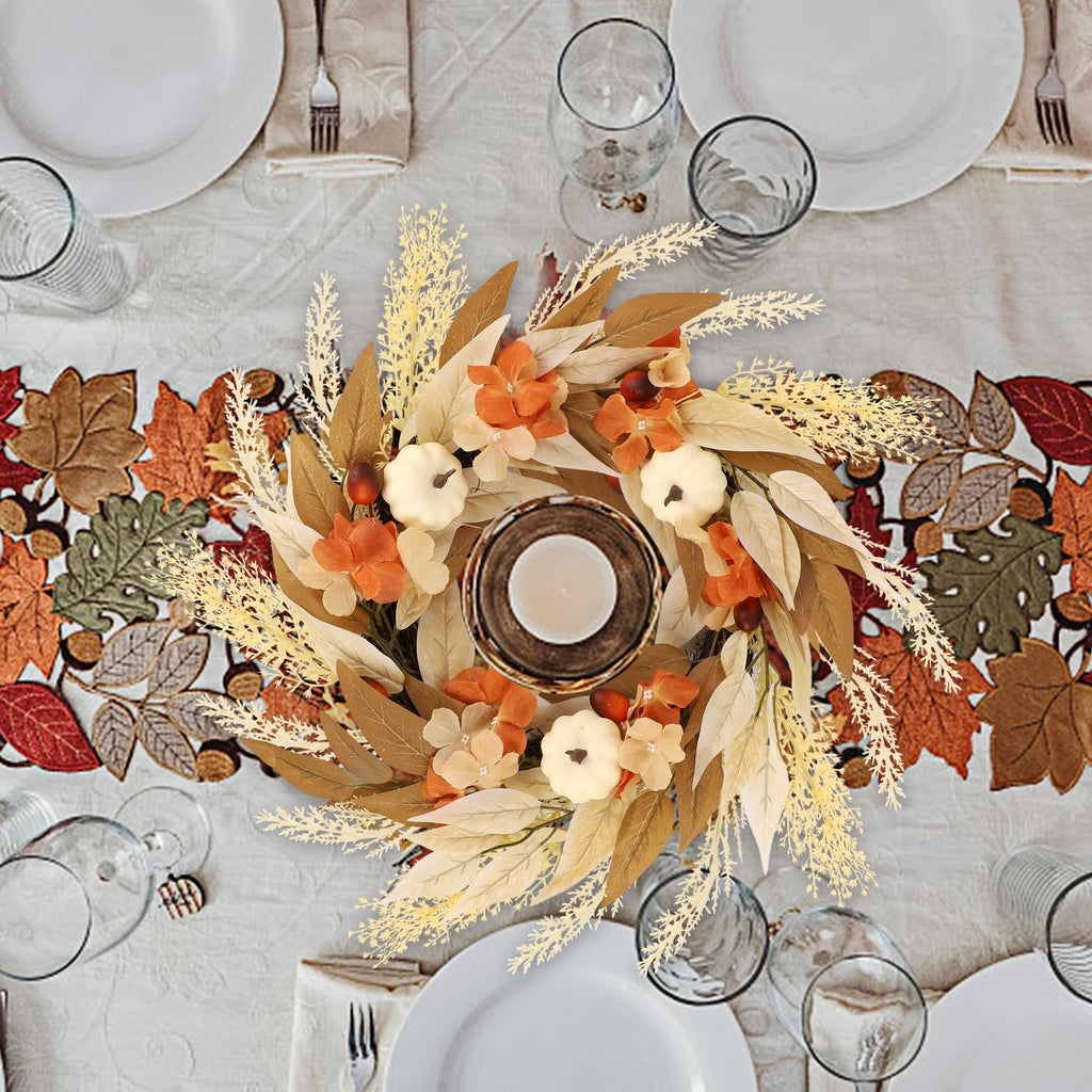 Artificial fall wreath with white pumpkins, orange flowers, and autumn leaves on a table setting