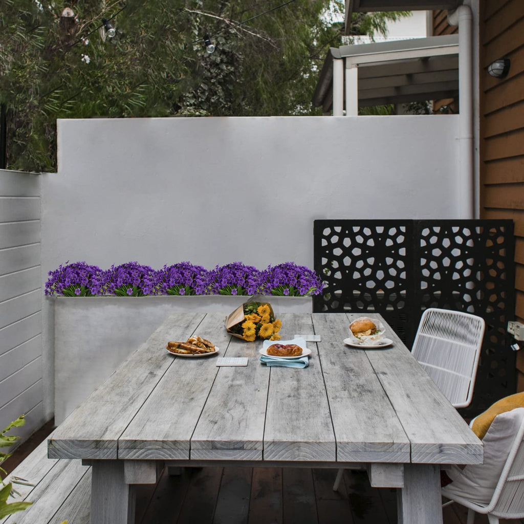 Outdoor dining table with purple flowers and food, set on a wooden deck.