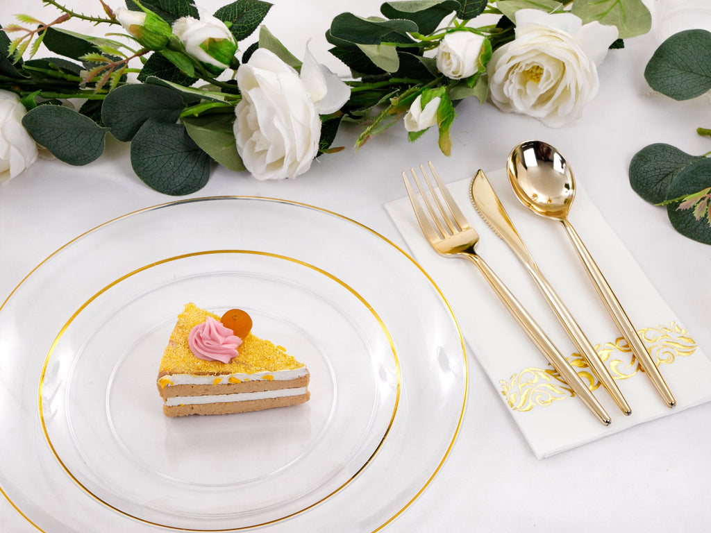 Clear plastic charger plate with gold rim holding a slice of cake, next to gold cutlery on a napkin and floral decor.