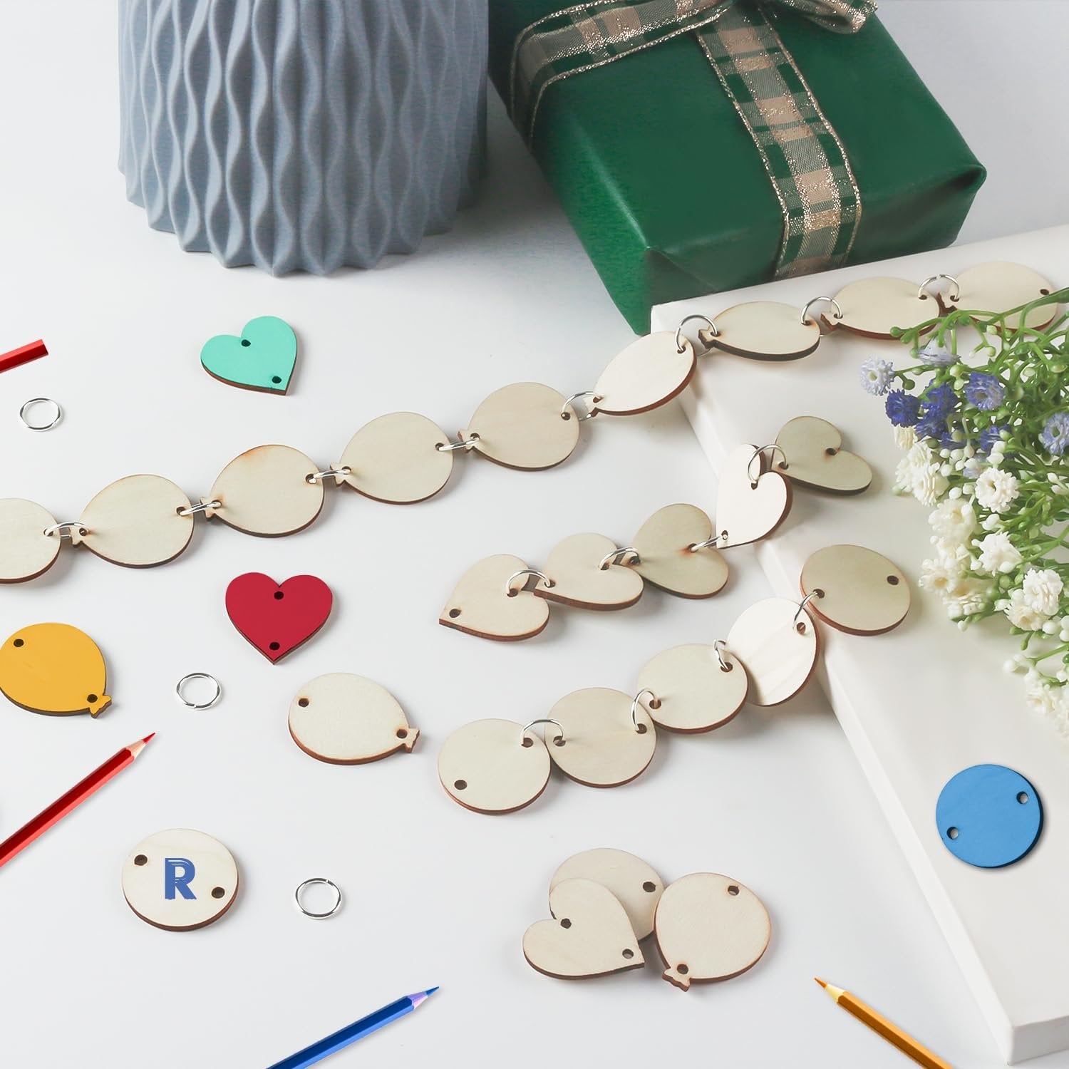 Wooden balloon and heart tags with rings, colored pencils, and a gift box on a white surface.