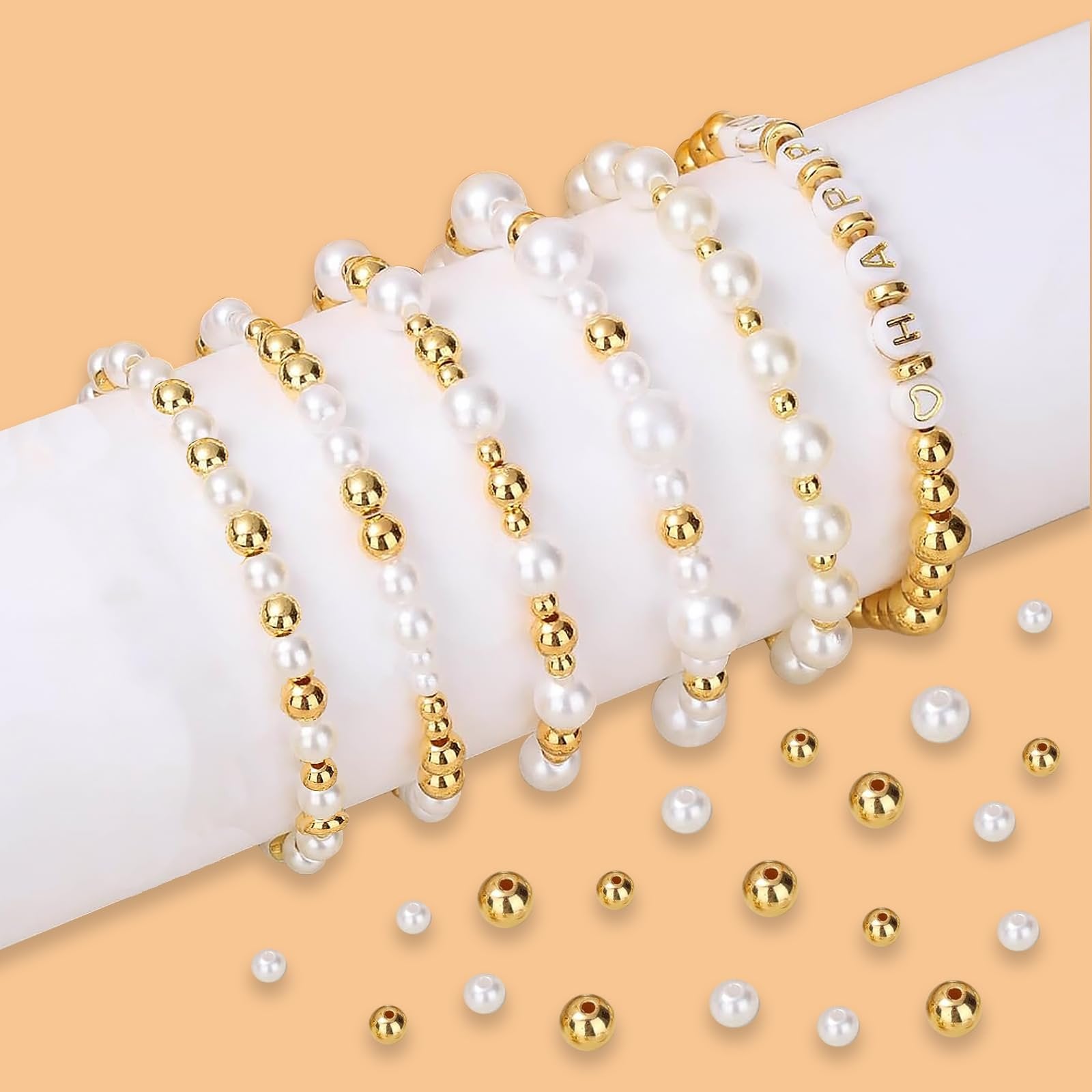 Several pearl and gold bead bracelets arranged on a white cylinder, with loose beads scattered around.