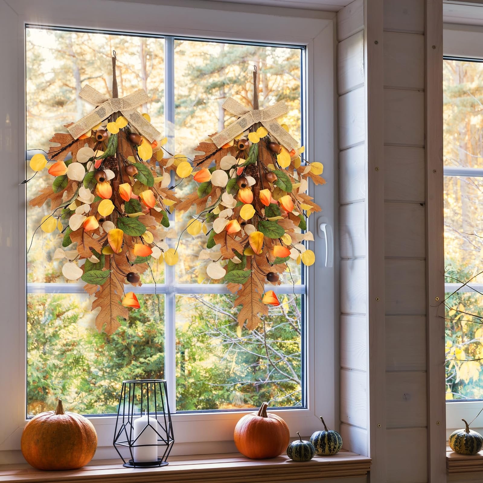 Two fall teardrop swag wreaths with golden eucalyptus and oak leaves hanging on a window.