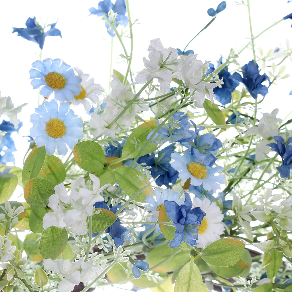 Close-up of artificial daisy wreath with blue and white wildflowers and green eucalyptus leaves.