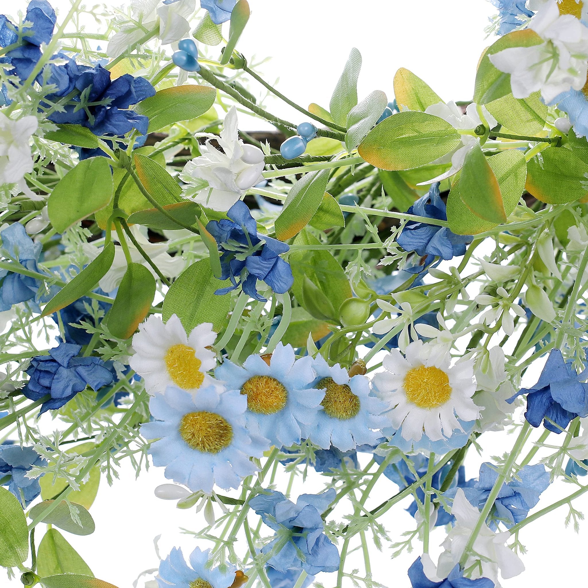 Close-up of an artificial wreath with blue, white, and yellow daisies, green leaves, and small blue berries against a white background.