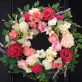 Front door wreath with red, pink, and white roses, dahlias, and greenery against a black door.