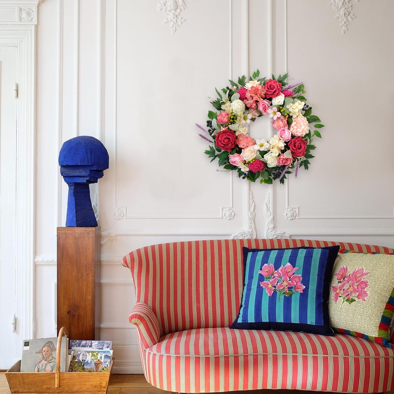 Floral wreath with roses and dahlias hanging on a wall above a striped sofa with decorative pillows.