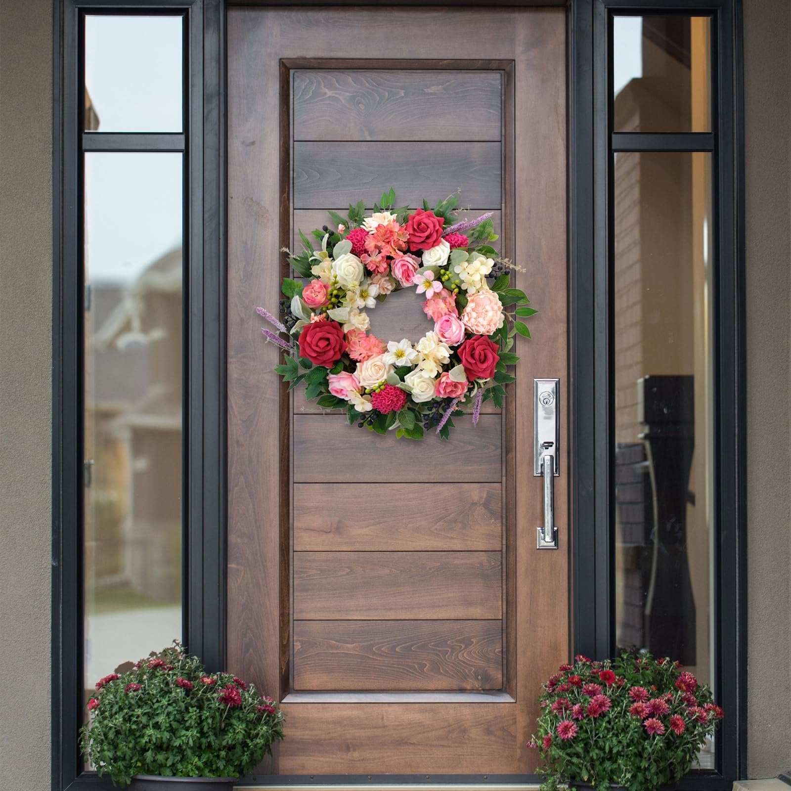 Floral wreath with red, pink, and cream roses and greenery hanging on a wooden front door.