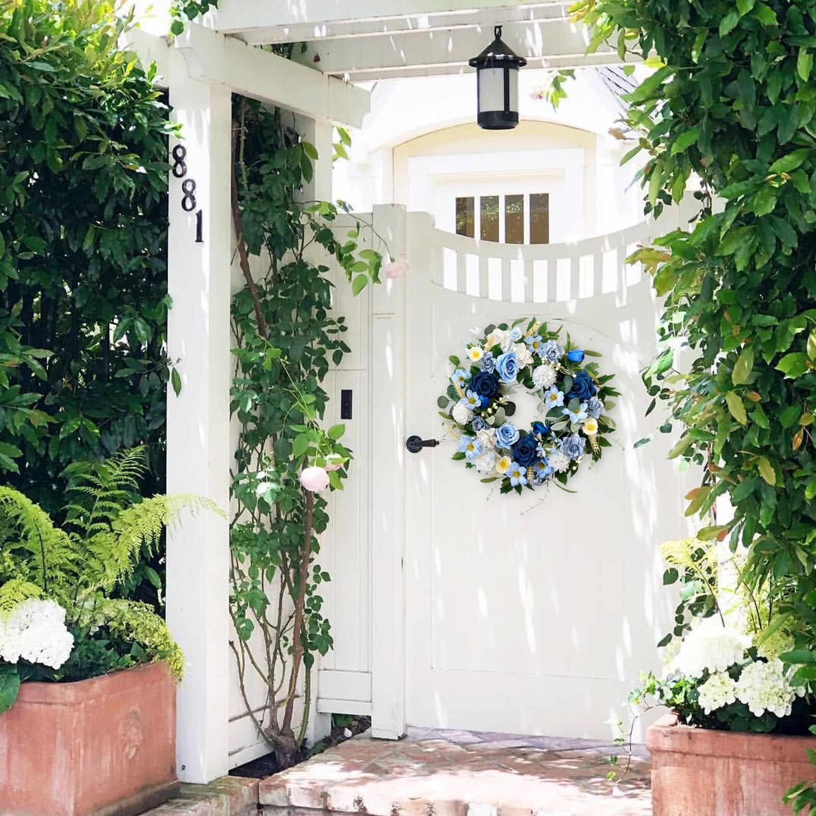 Blue floral wreath with roses and hydrangeas hanging on a white door, surrounded by greenery.