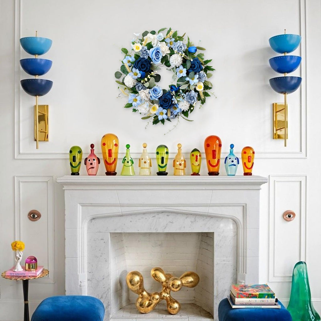 Blue and white floral wreath with green leaves hanging above a fireplace with decorative glass figures.
