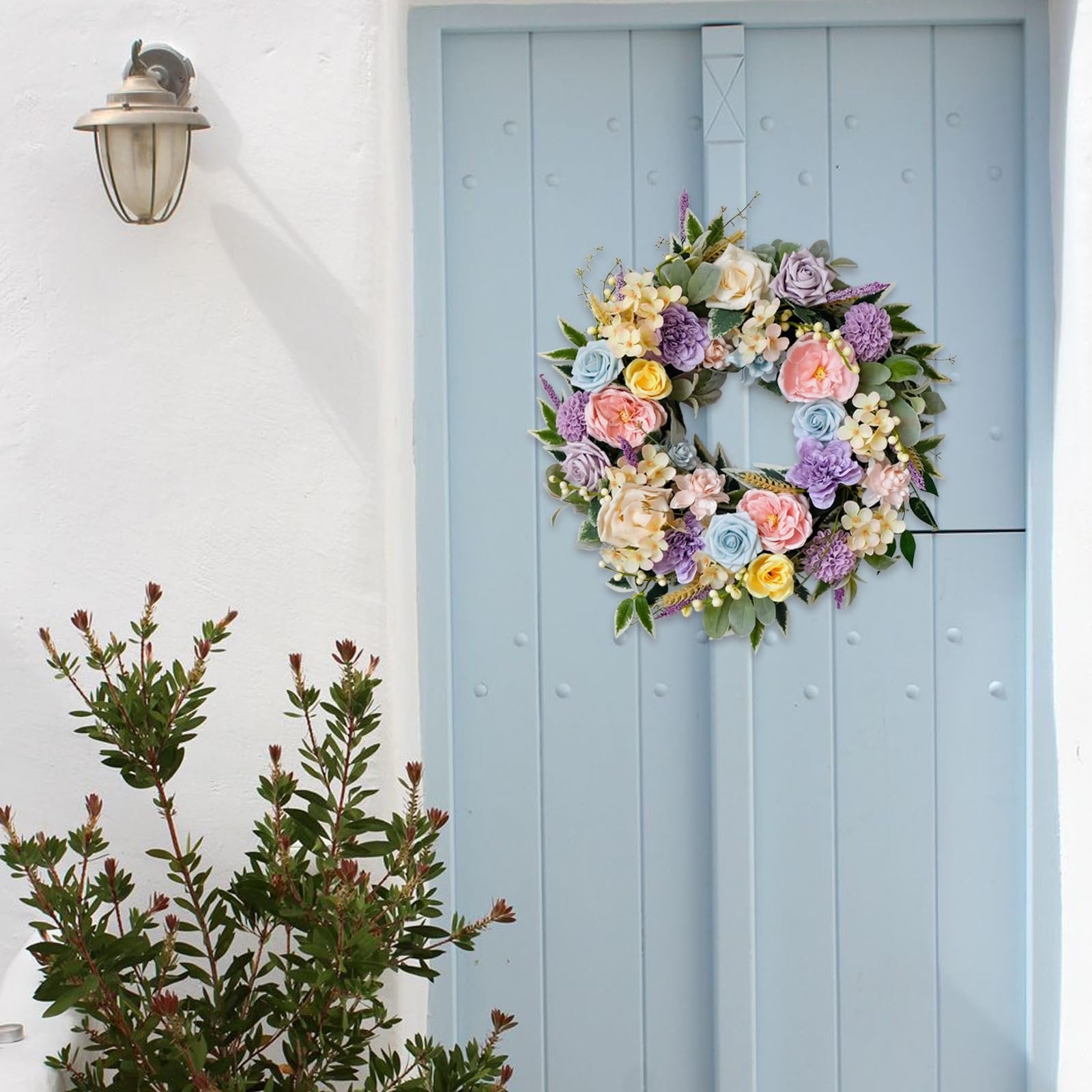 Floral wreath with roses, peonies, hydrangeas, and leaves hanging on a light blue door.