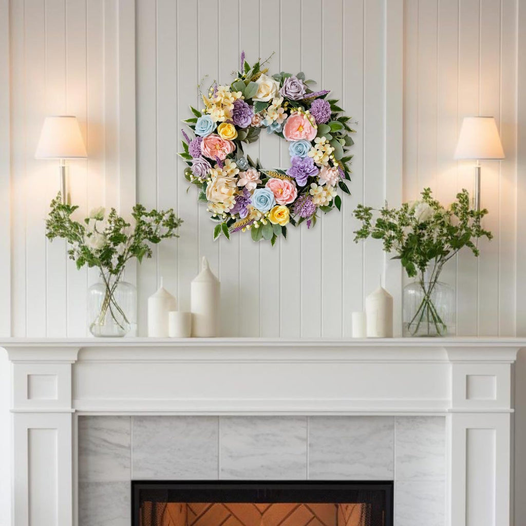 Floral wreath with roses, peonies, hydrangeas, and leaves hanging on a white paneled wall above a fireplace.