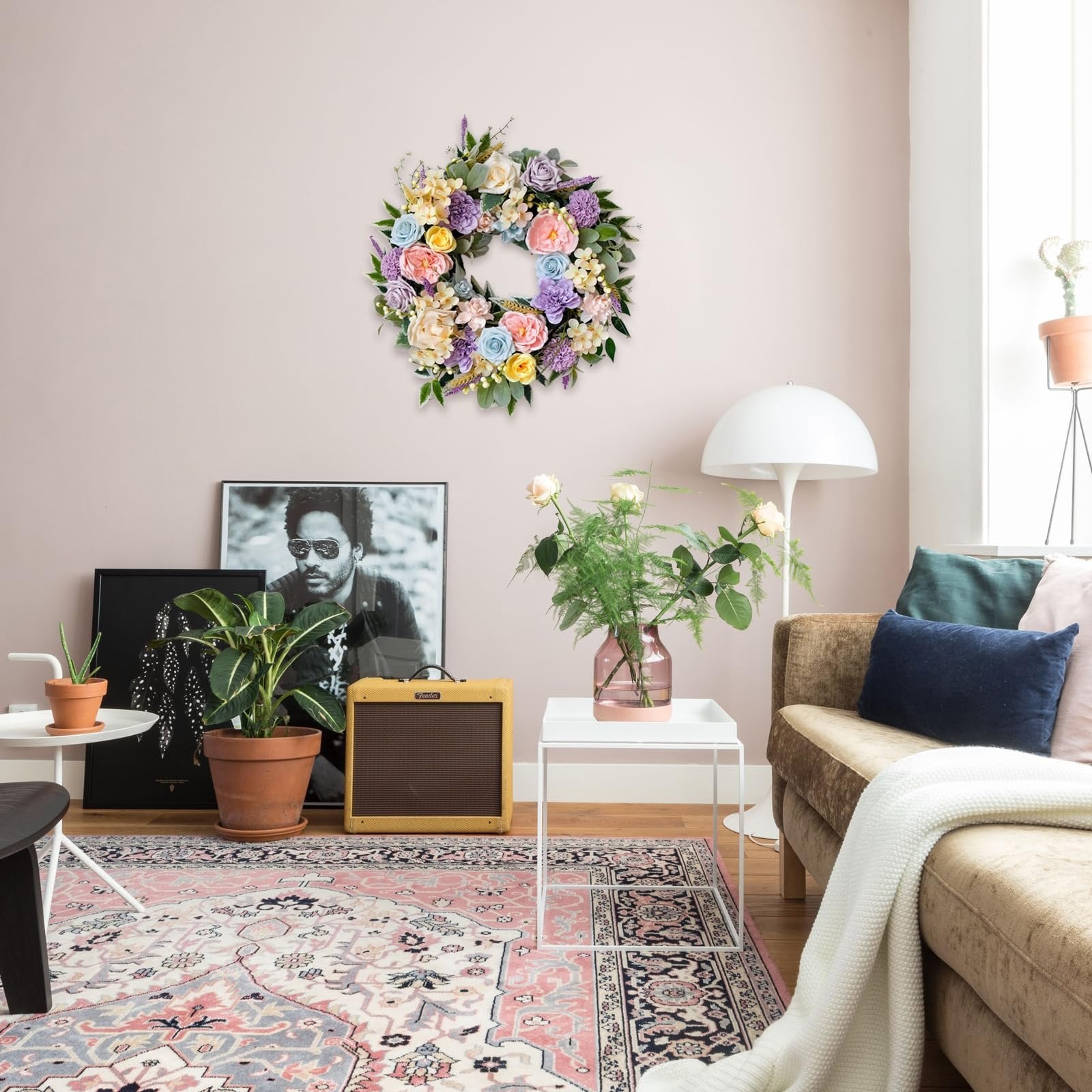 Floral wreath with roses, peonies, hydrangeas, and leaves hanging on a wall above a sofa and rug.