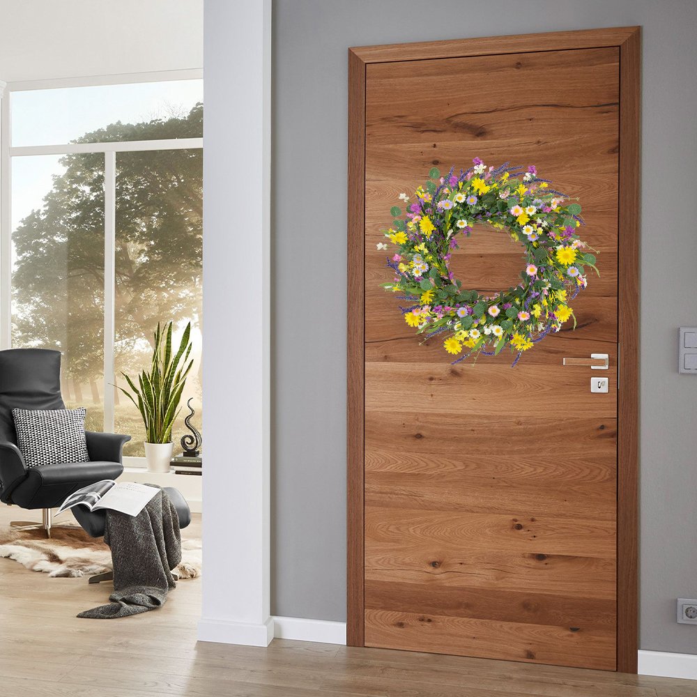 Artificial spring wreath with daisies, lavender, jasmine, and wildflowers on a grapevine base, hanging on a wooden door.