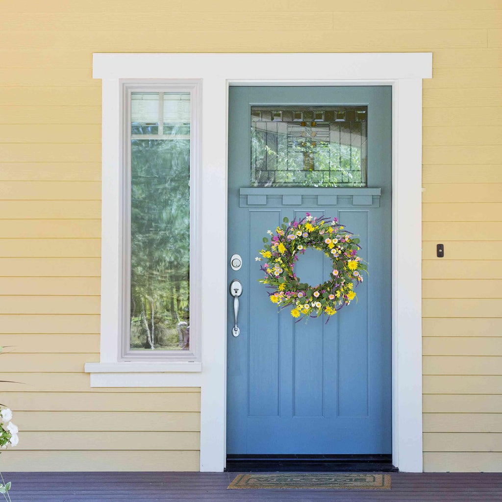 Artificial spring wreath with daisies, lavender, jasmine, and wildflowers on a grapevine base hanging on a blue front door.