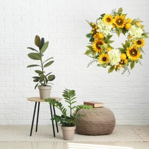 Artificial sunflower wreath with hydrangeas, lemons, and berries hanging on a white brick wall.