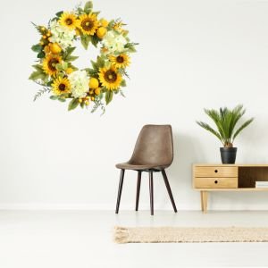 Artificial sunflower wreath with hydrangeas, lemons, and berries hanging on a white wall above a chair and cabinet.