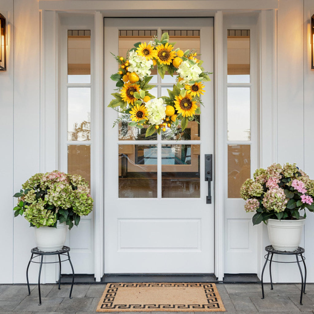 Artificial sunflower wreath with hydrangeas, lemons, and berries hanging on a white front door.