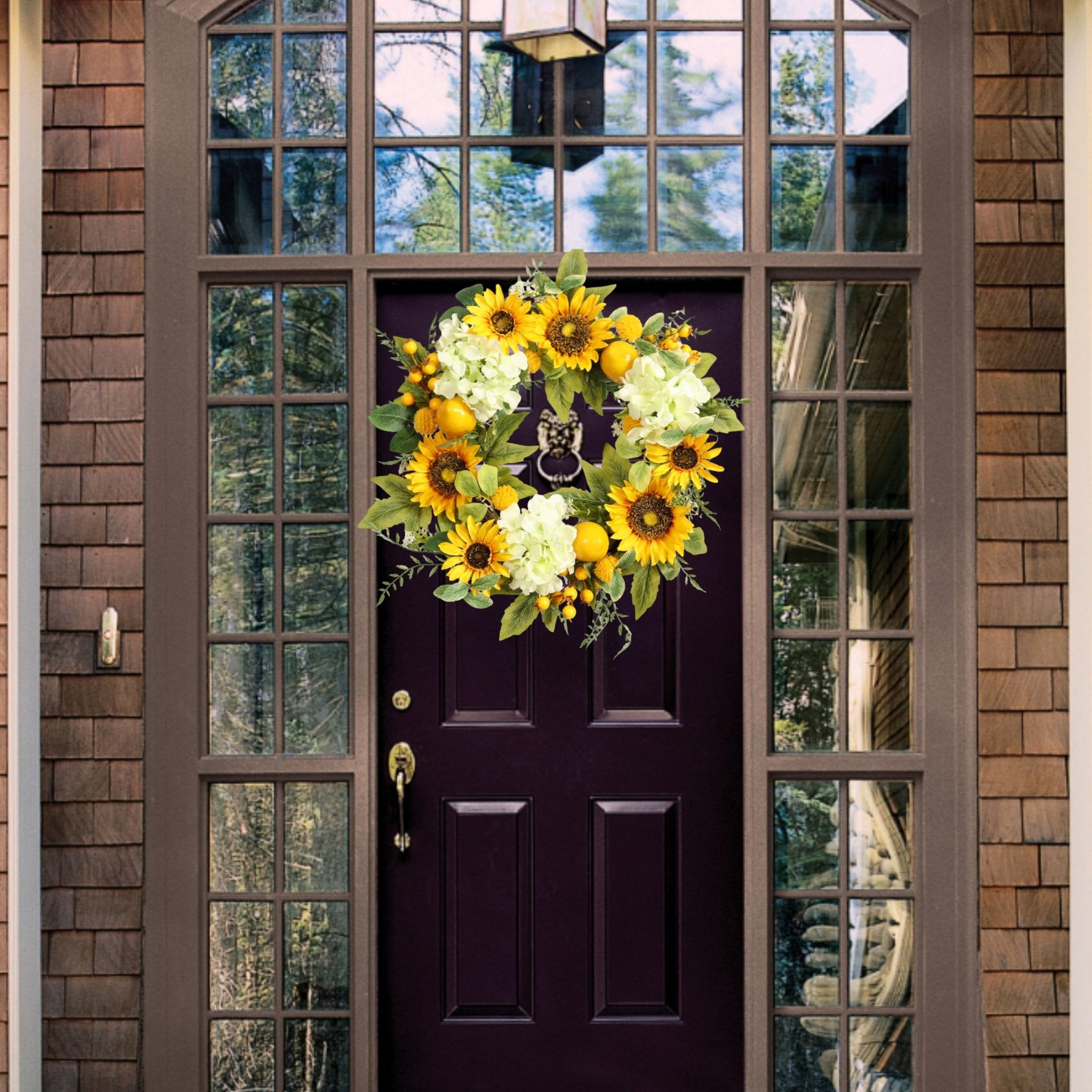 Artificial sunflower wreath with hydrangeas, lemons, and berries hanging on a dark purple front door.