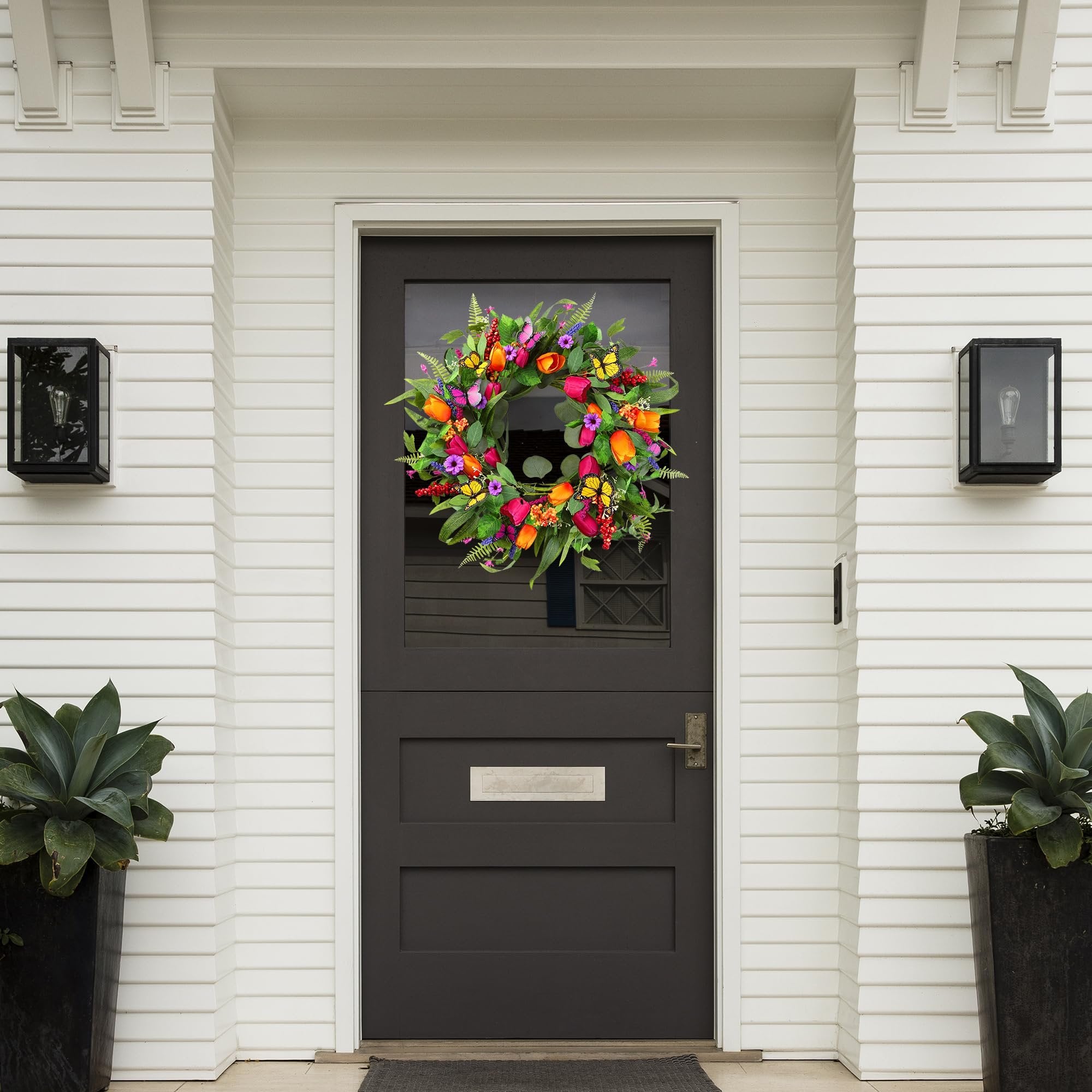 Colorful artificial tulip wreath with silk greenery and butterflies hanging on a dark front door.