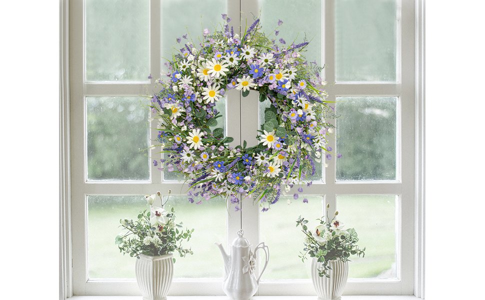 Blue summer wreath with daisies, lavender, and eucalyptus hanging on a white window frame with two potted plants below.