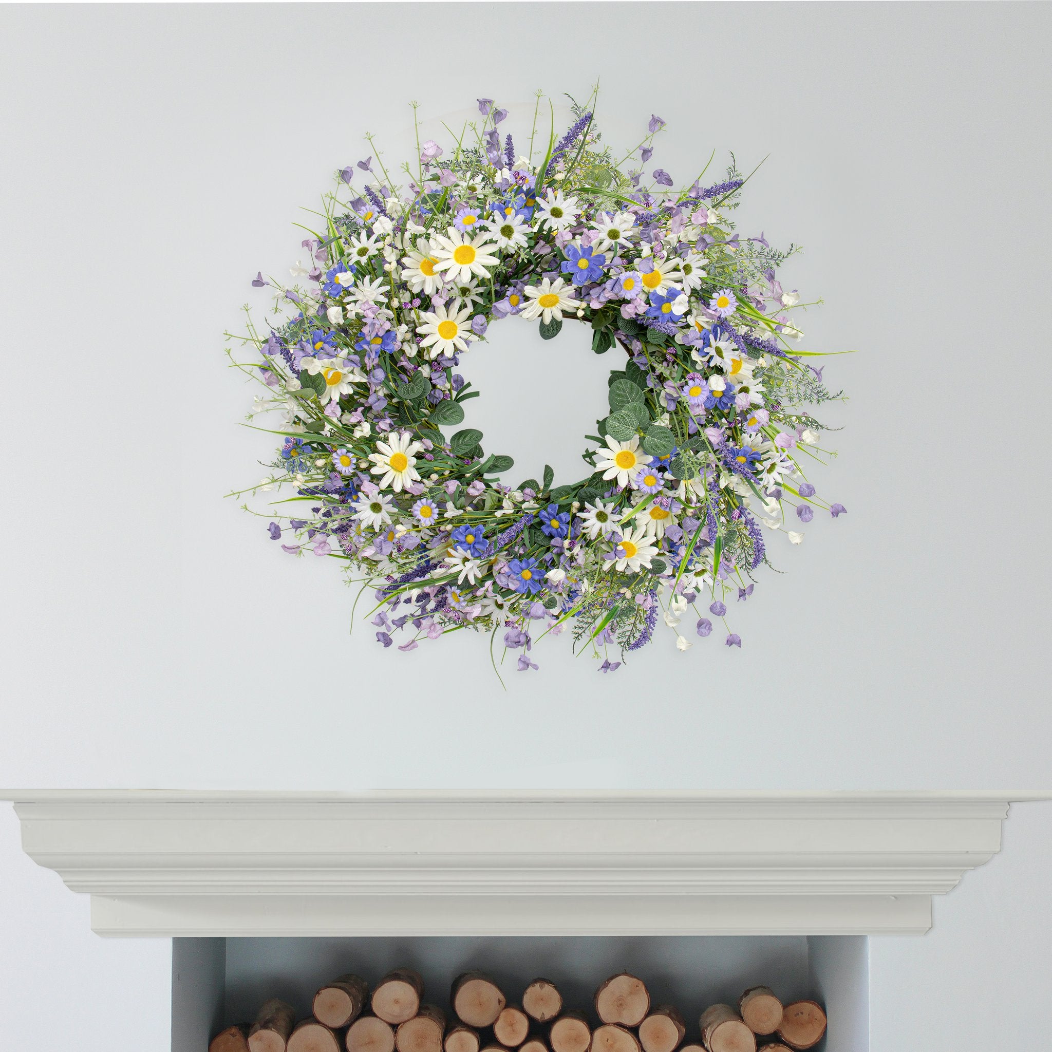 22-inch blue summer wreath with daisies, lavender, wildflowers, and eucalyptus hanging on a wall above a fireplace.