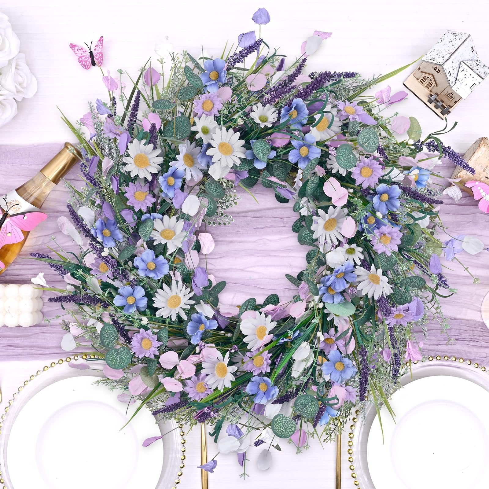 Spring daisy and lavender wreath with eucalyptus on a table setting with plates and a champagne bottle.