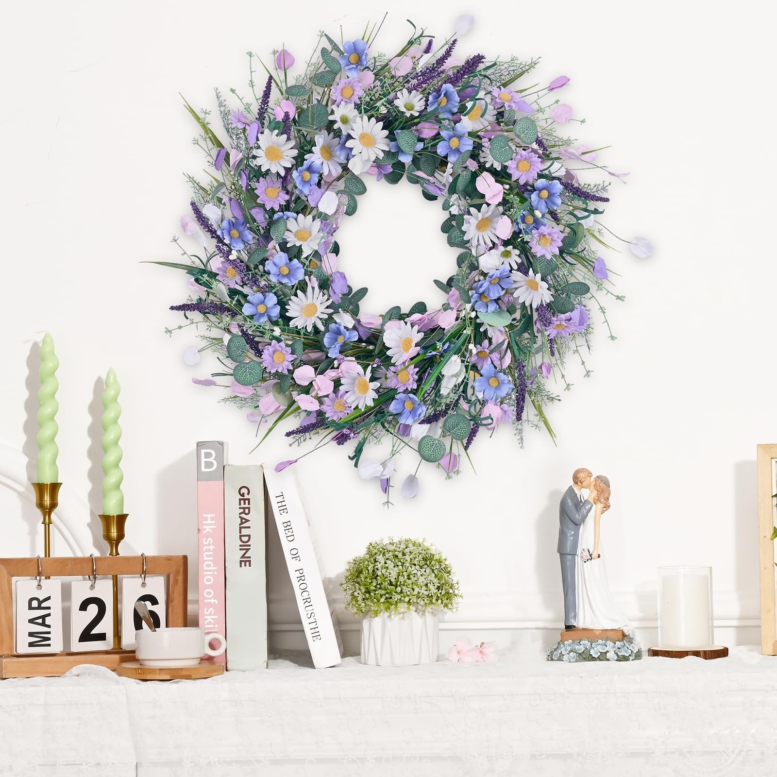 Spring daisy and lavender wreath with eucalyptus leaves hanging on a white wall above decorative items.