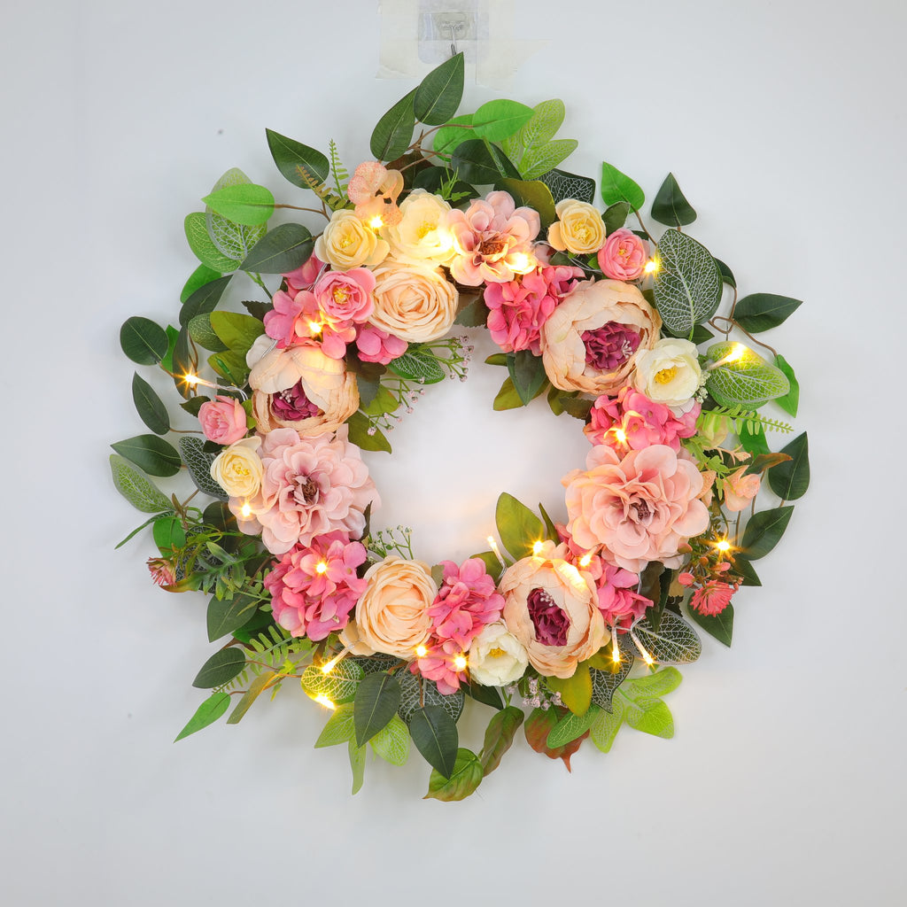 Lighted floral wreath with pink and cream peonies, hydrangeas, and roses on a white background.
