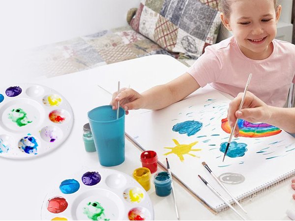 Two children painting at a table with round plastic paint palettes and art supplies
