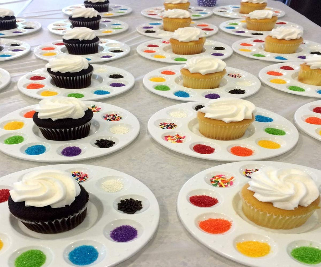 Cupcakes with white frosting on paint palettes filled with colorful sprinkles and sanding sugar.