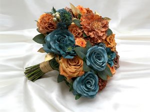 Teal and orange artificial flower bouquet with green leaves and gold accents, tied with twine on a white satin background.