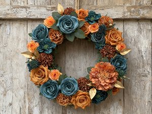 Teal and orange artificial flower wreath with gold accents hanging on a wooden door