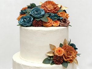 Teal and orange artificial silk flowers arranged on a white cake