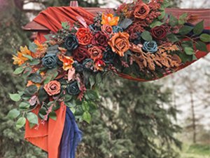 Artificial silk flower arrangement in teal, orange, and rust colors draped over a wooden arch with greenery.