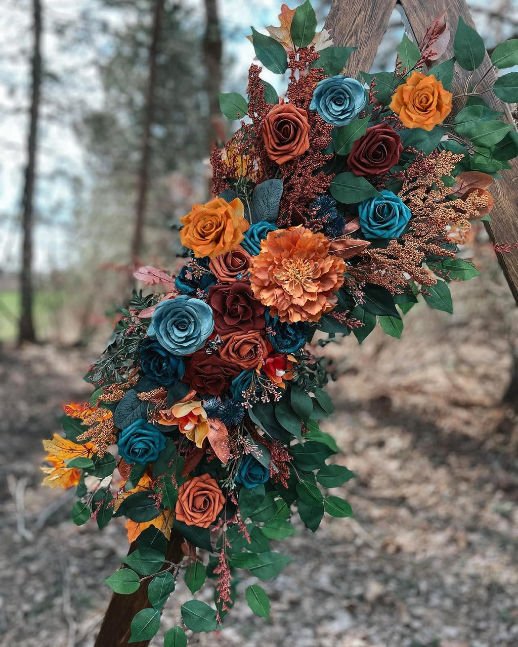 Artificial floral arrangement with teal, orange, and rust roses and greenery on a wooden arch