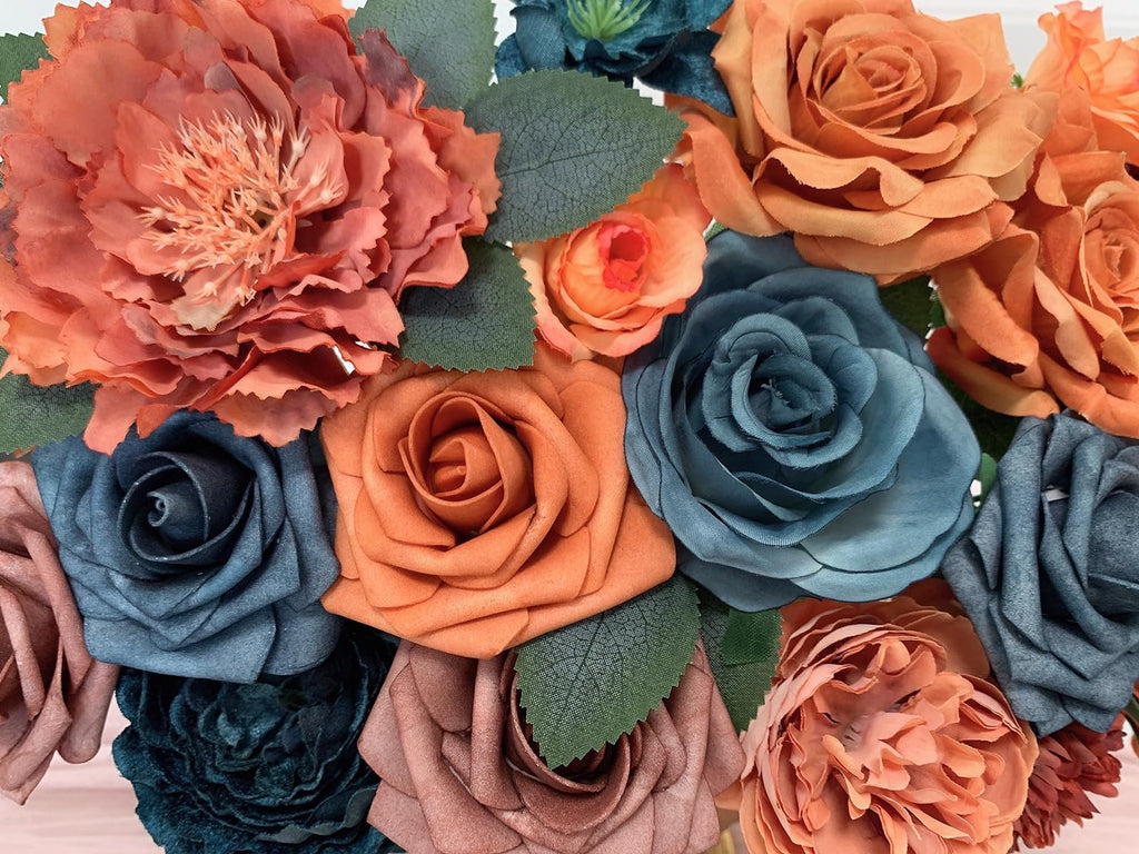 Close-up of a bouquet of artificial silk flowers in teal, orange, and dusty rose colors with green leaves.