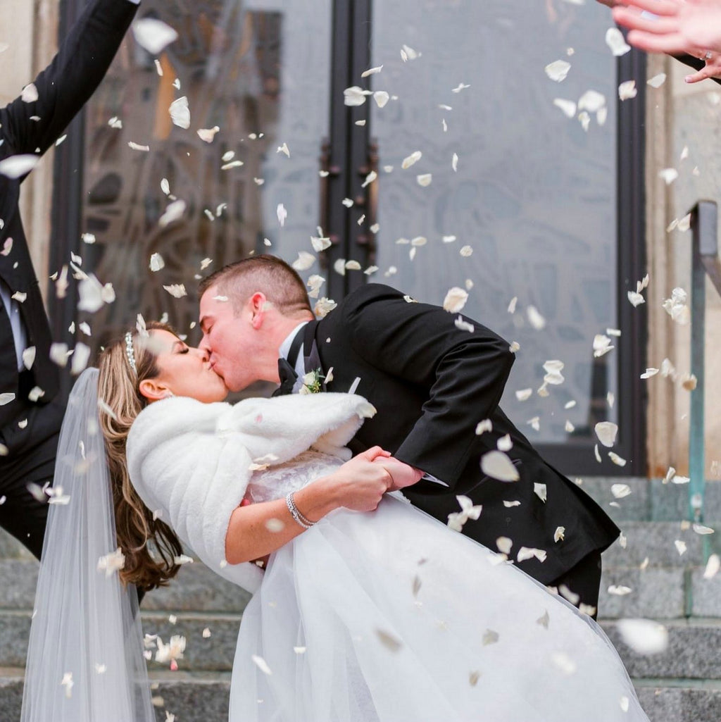 Bride and groom kissing while petals fall around them on wedding day