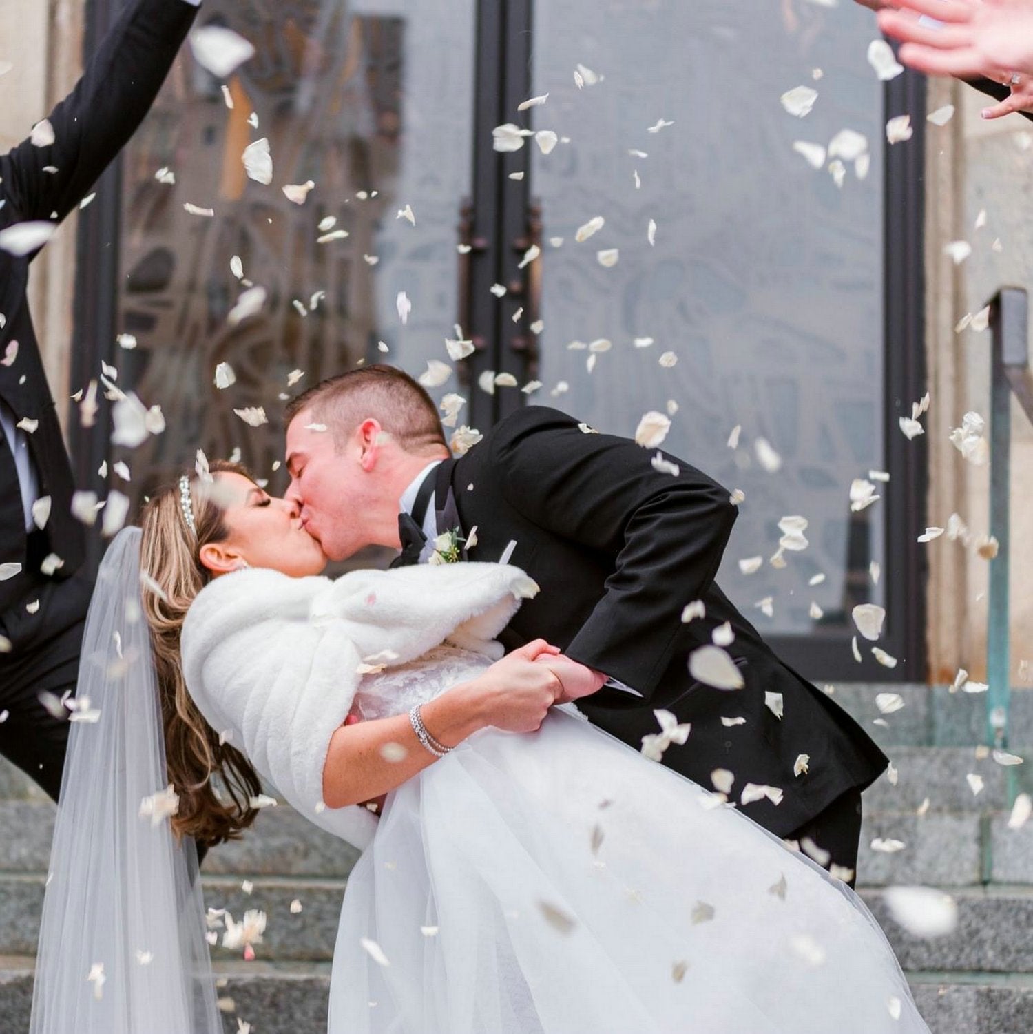 Bride and groom kissing while petals fall around them on wedding day