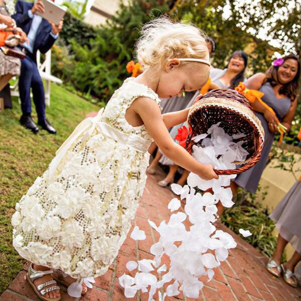 Flower girl in a white dress scattering white petals from a basket at a wedding ceremony