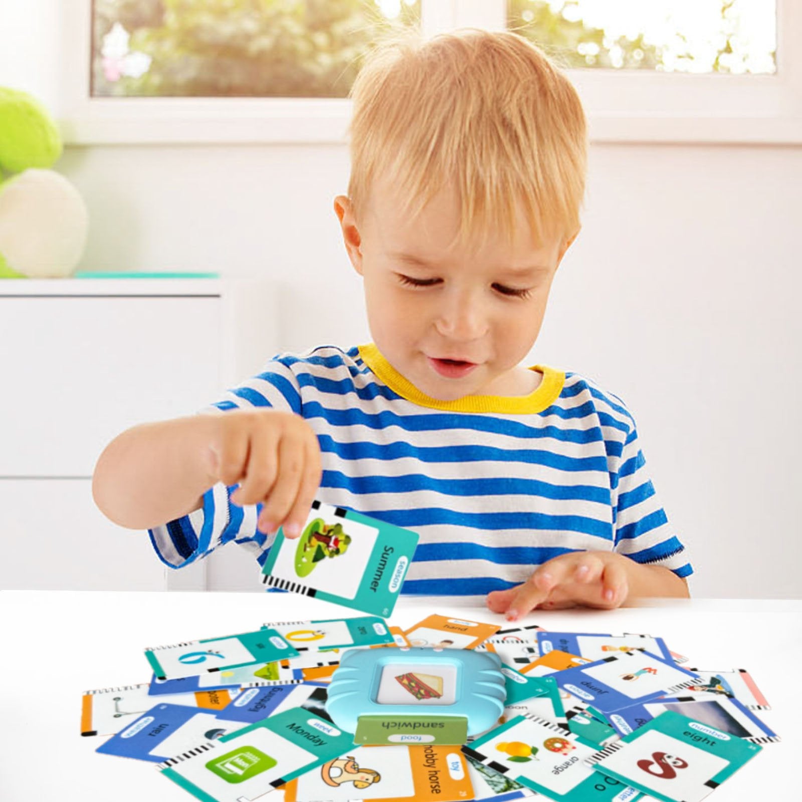 Toddler boy playing with talking flash cards and reader device on a white table.