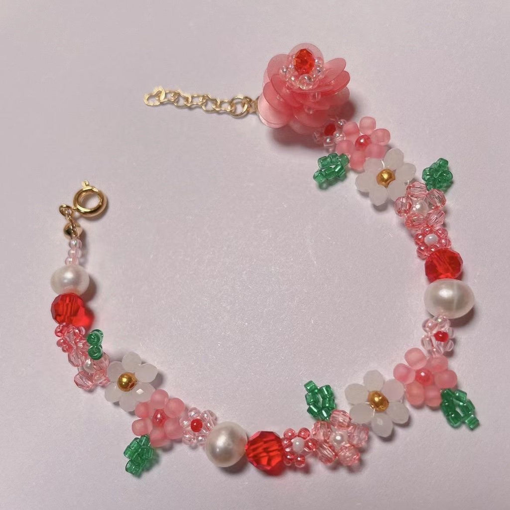 Beaded bracelet with pink flowers, white pearls, and red beads on a white background
