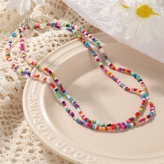Two strands of colorful seed bead necklaces with pearl accents laid on a decorative plate.