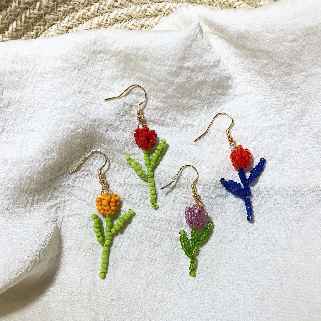 Four colorful beaded flower dangle earrings on a white textured fabric background