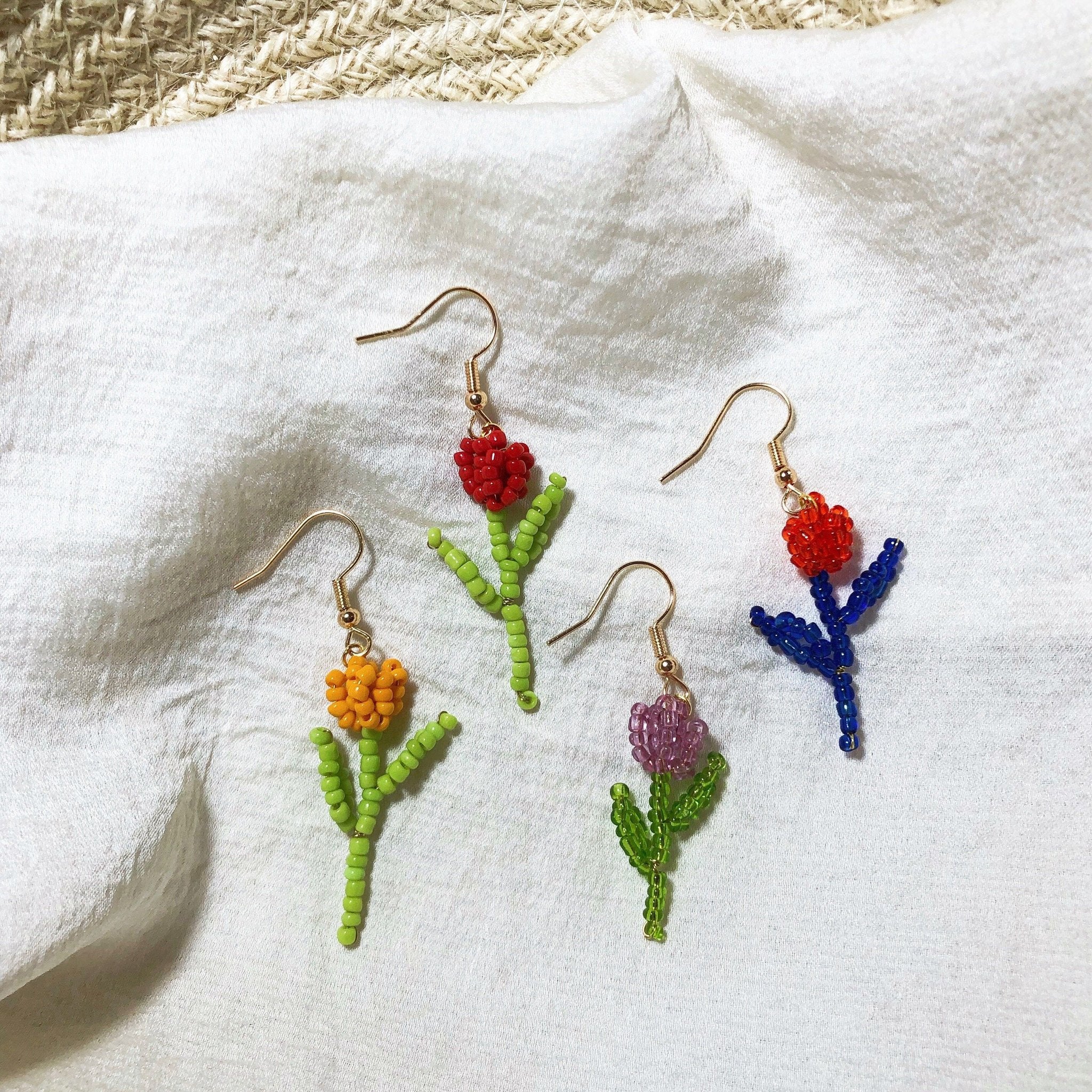 Four colorful beaded flower dangle earrings on a white textured fabric background