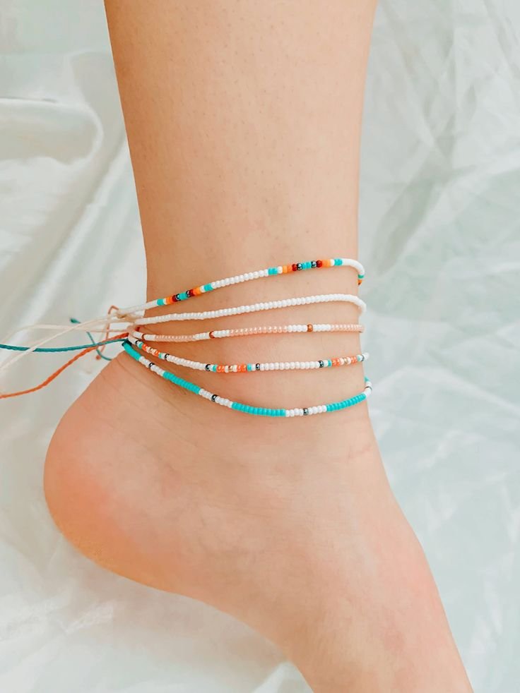 Ankle adorned with multiple colorful seed bead bracelets, including white, turquoise, orange, and pink beads.