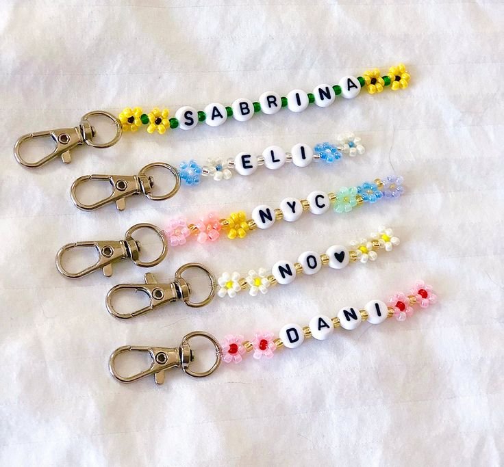 Five beaded keychains with letter beads spelling names and flower accents, attached to lobster clasps.