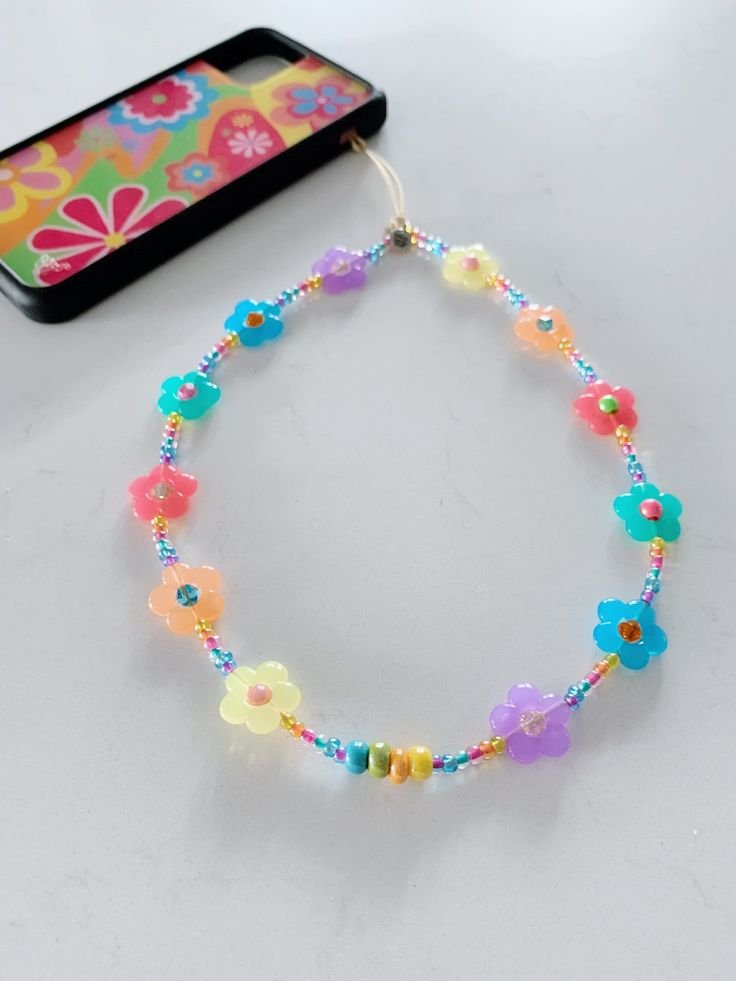 Colorful beaded phone charm with flower shapes and small beads, attached to a phone case with a retro floral pattern.